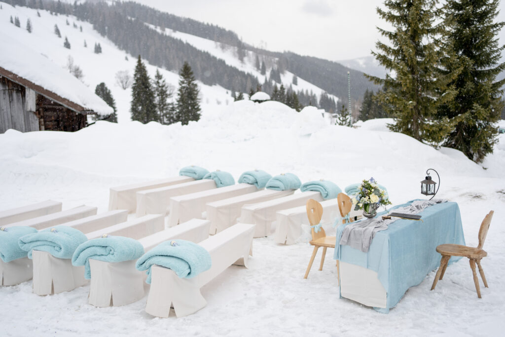 Outdoor Wedding Ceremony Set up in the mountains, cream benches with blue blankets are set amongst the snowy mountains