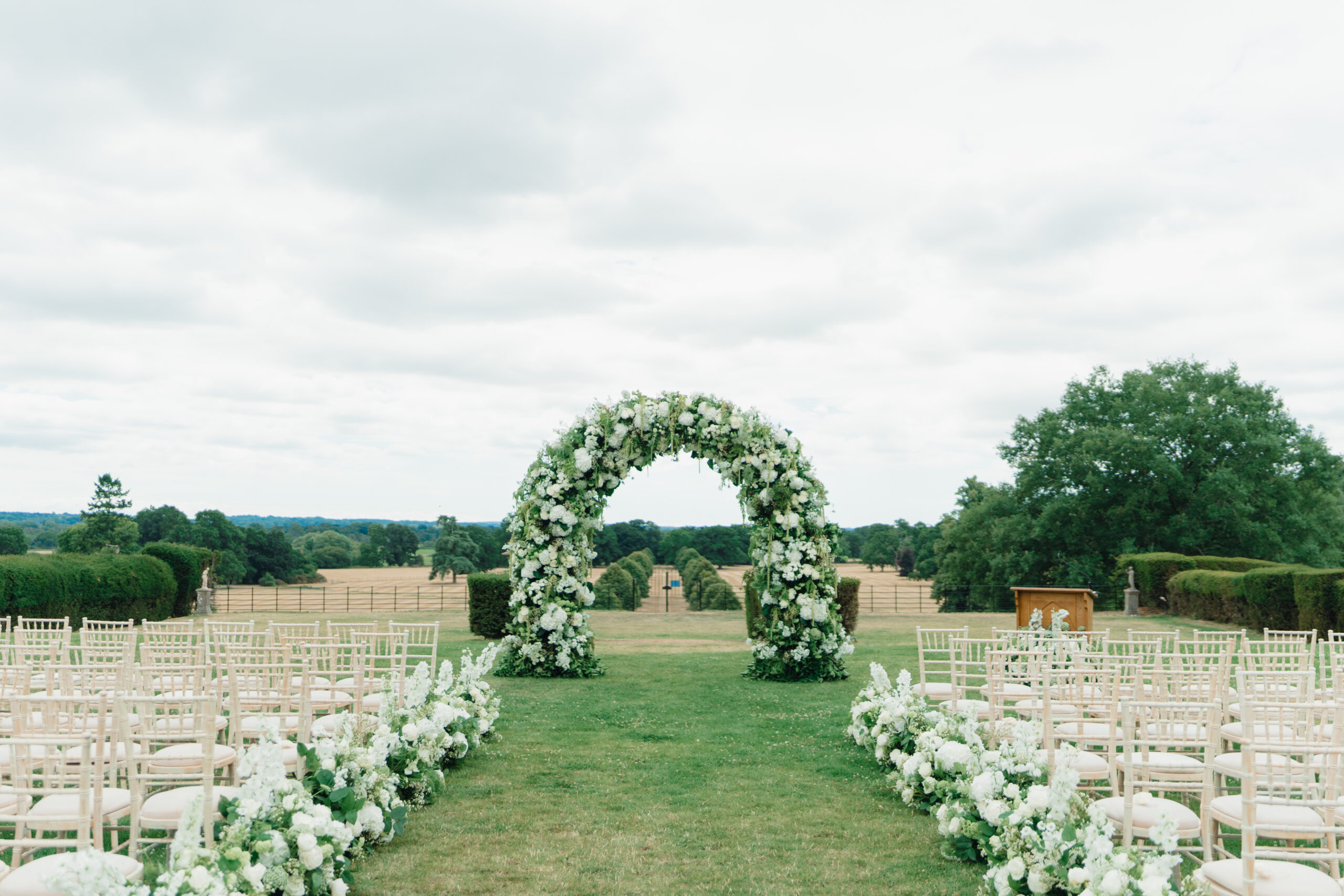 Outside English countryside wedding set up with green and white floral arch