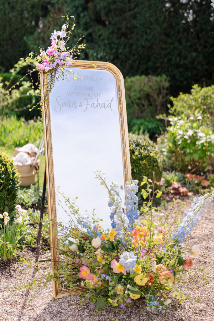 A mirrored welcome sign with summer florals for a short notice wedding planned at Four Seasons Hampshire by Ella Hartig
