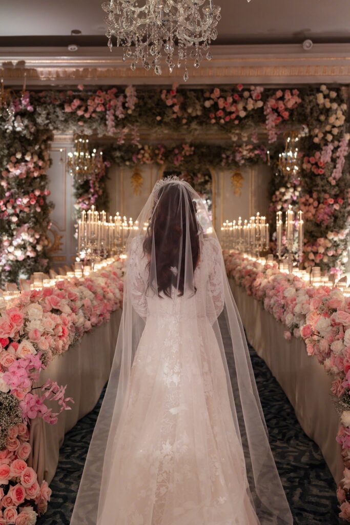 A bride stands among 12000 roses in her pink floral wedding reception, a short notice wedding planned at Mandarin Oriental by Ella Hartig